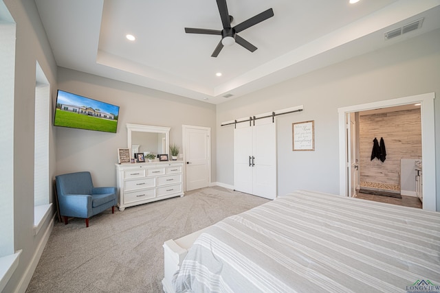 carpeted bedroom with ceiling fan, a barn door, and a raised ceiling