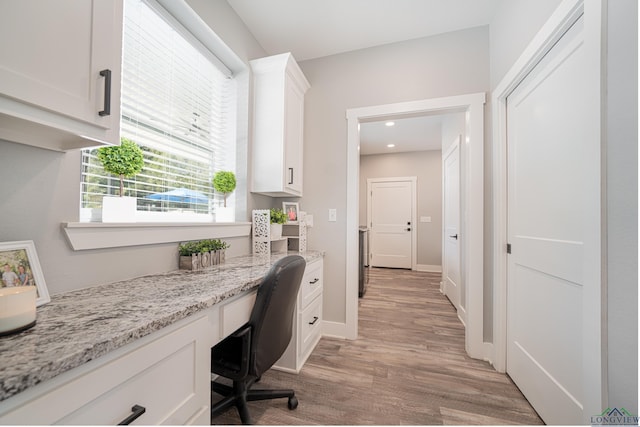 office featuring built in desk, light hardwood / wood-style floors, and a healthy amount of sunlight