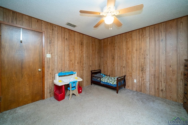 bedroom featuring a textured ceiling, carpet floors, ceiling fan, and wood walls