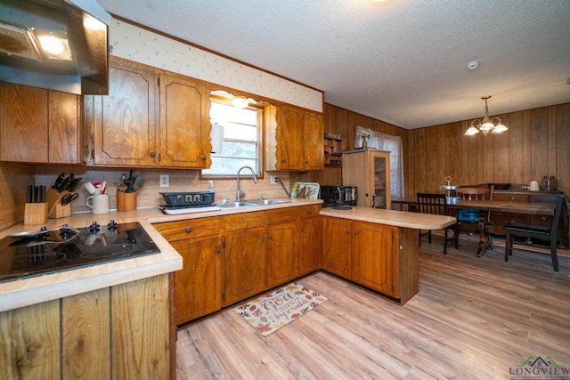 kitchen with kitchen peninsula, black electric cooktop, sink, pendant lighting, and a notable chandelier