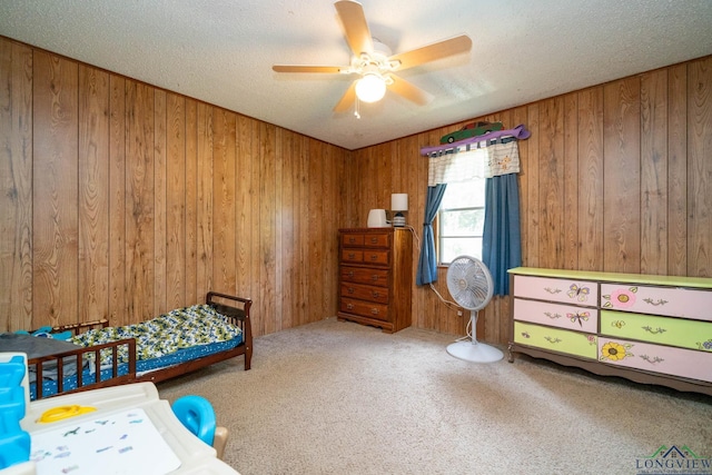 carpeted bedroom with ceiling fan, wood walls, and a textured ceiling