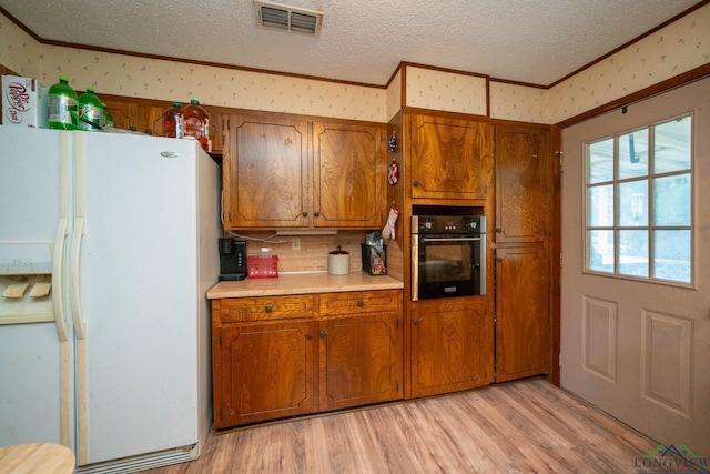 kitchen featuring wall oven, ornamental molding, a textured ceiling, white refrigerator with ice dispenser, and light hardwood / wood-style floors