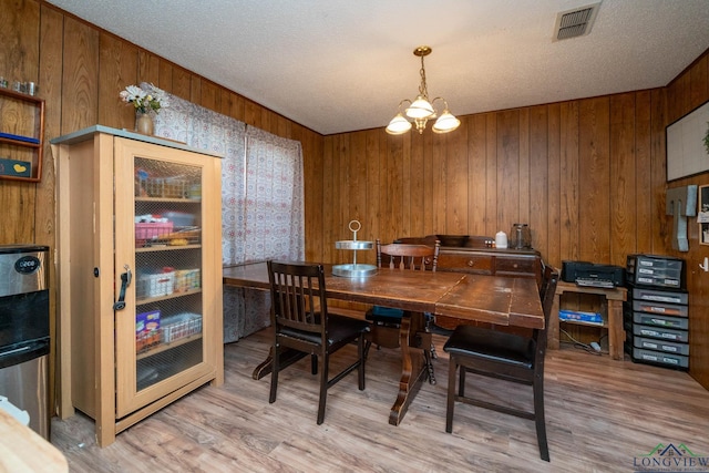 dining space featuring wood walls, light wood-type flooring, a textured ceiling, and a notable chandelier