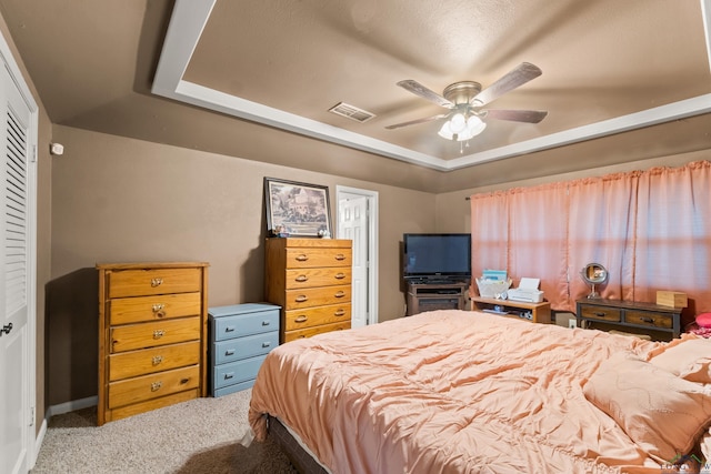 carpeted bedroom with a closet, a tray ceiling, and ceiling fan