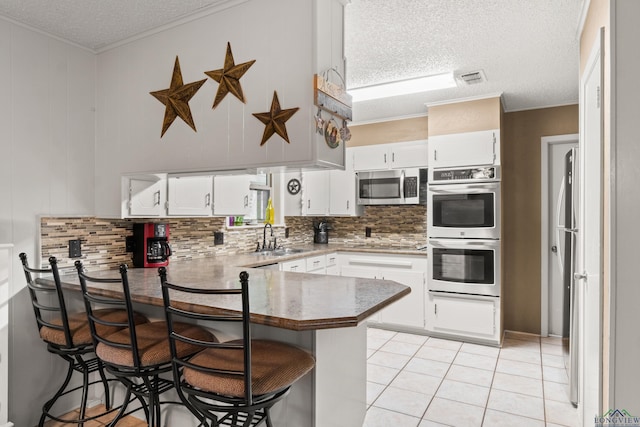 kitchen with stainless steel appliances, kitchen peninsula, a textured ceiling, a breakfast bar, and white cabinets