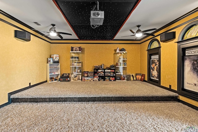 carpeted home theater room with ceiling fan and crown molding