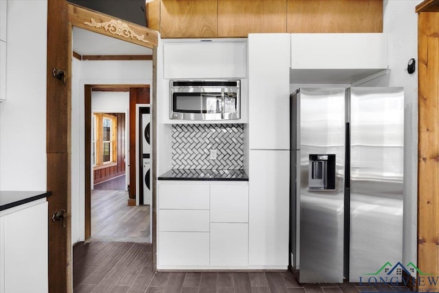 501 S Harrison St, Longview, TX 75601 - kitchen with appliances with stainless steel finishes, stacked washer and clothes dryer, dark countertops, white cabinetry, and tasteful backsplash