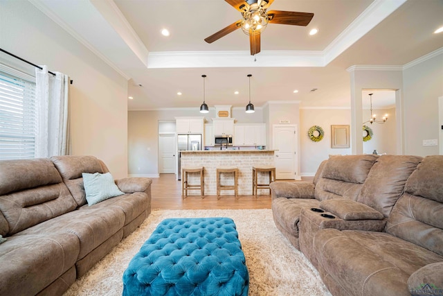 living area with baseboards, light wood-style floors, ceiling fan with notable chandelier, and a raised ceiling