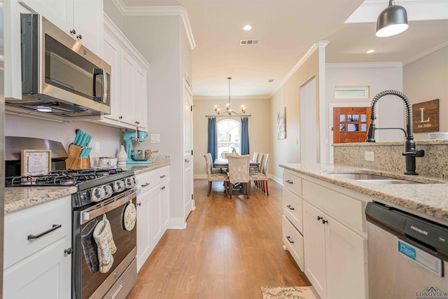 kitchen with a sink, stainless steel appliances, white cabinets, ornamental molding, and visible vents