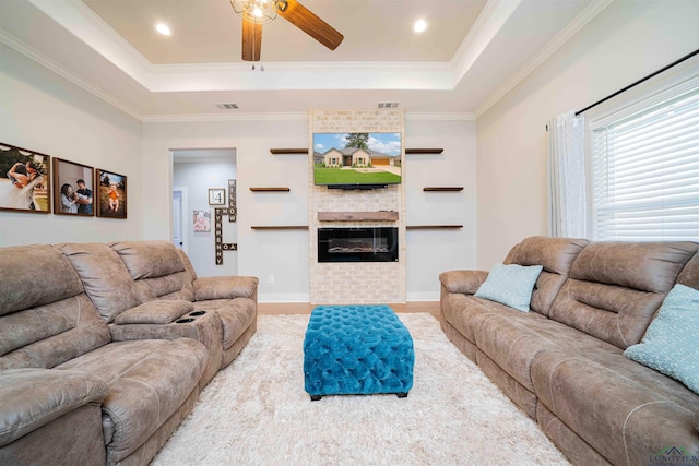 living area with a tray ceiling, wood finished floors, visible vents, ornamental molding, and ceiling fan