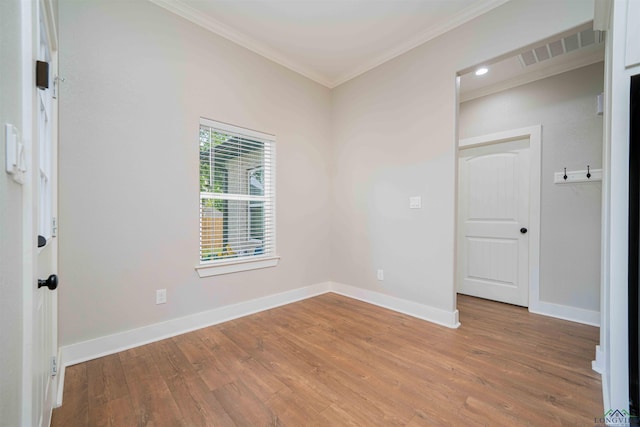 empty room with baseboards, crown molding, wood finished floors, and visible vents