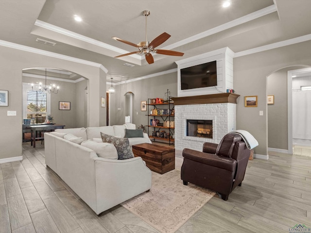 living room featuring crown molding, a tray ceiling, a fireplace, and ceiling fan with notable chandelier