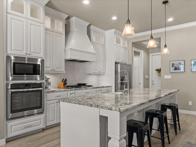 kitchen featuring stainless steel appliances, an island with sink, custom range hood, and white cabinets