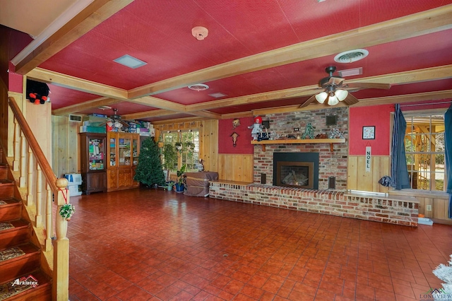 living room with wooden walls, a brick fireplace, ceiling fan, beamed ceiling, and plenty of natural light