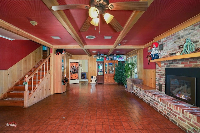 unfurnished living room with beam ceiling, ceiling fan, coffered ceiling, a brick fireplace, and wood walls