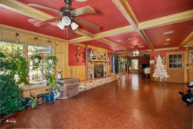 unfurnished living room featuring wooden walls, ceiling fan, ornamental molding, a fireplace, and beamed ceiling