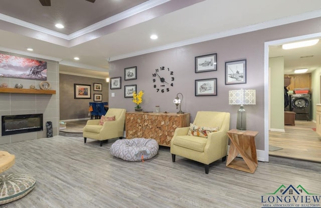 living room featuring ceiling fan, a fireplace, crown molding, washing machine and clothes dryer, and light hardwood / wood-style flooring