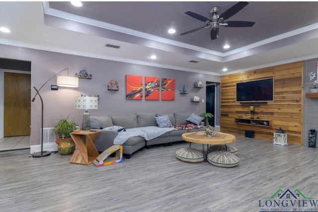 living room with ceiling fan, hardwood / wood-style floors, crown molding, a tray ceiling, and wooden walls