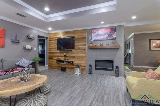 living room featuring wooden walls, a tile fireplace, crown molding, and wood-type flooring