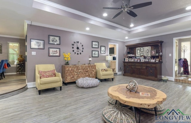 living room with ceiling fan, wood-type flooring, a tray ceiling, and crown molding