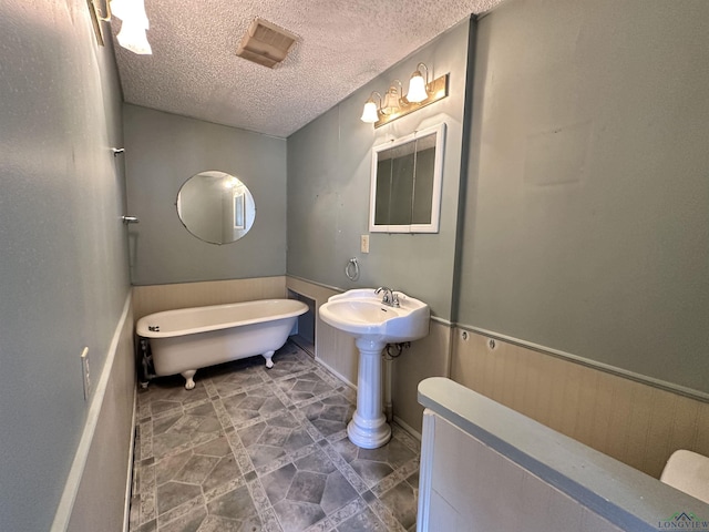 587 Floyd Evans Rd, Marshall, TX 75672 - bathroom featuring a soaking tub, wainscoting, a textured ceiling, and visible vents