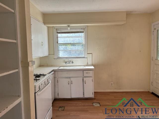 kitchen featuring white cabinets, gas range, light wood-type flooring, and sink