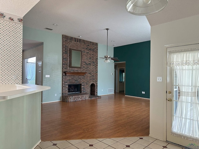 unfurnished living room featuring light hardwood / wood-style floors, a brick fireplace, and a textured ceiling