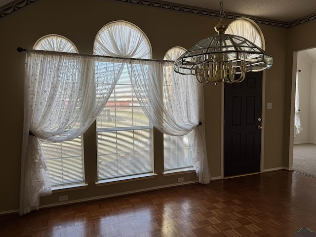 unfurnished dining area featuring a notable chandelier, dark parquet floors, and a textured ceiling