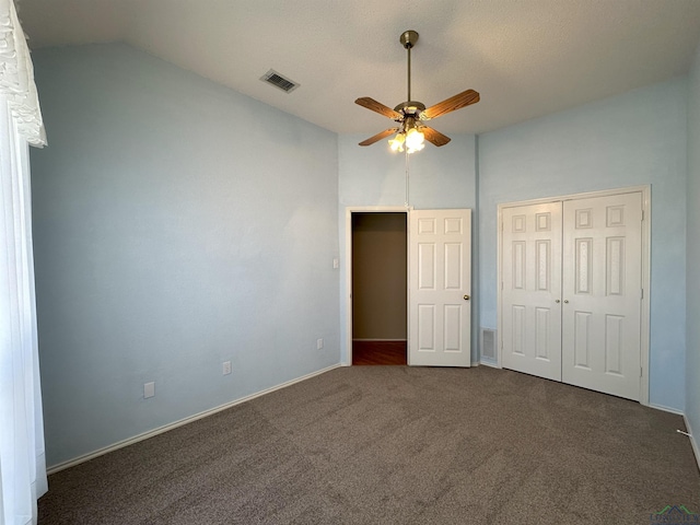 unfurnished bedroom with vaulted ceiling, a closet, ceiling fan, and dark colored carpet