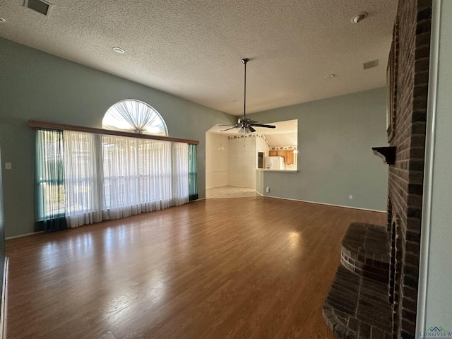 unfurnished living room with wood-type flooring, a textured ceiling, ceiling fan, and a fireplace