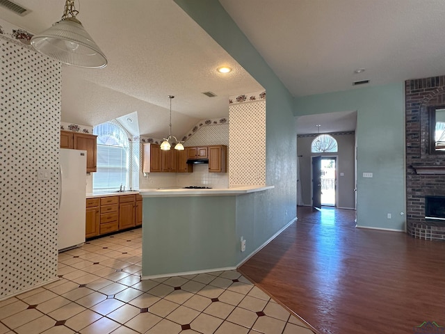 kitchen with lofted ceiling, sink, a brick fireplace, white refrigerator, and pendant lighting