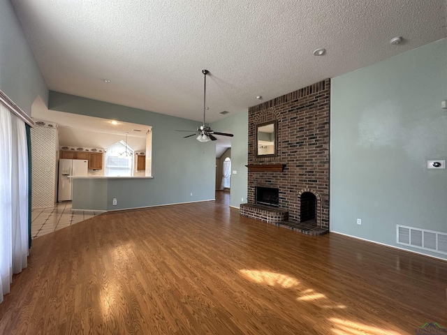 unfurnished living room with ceiling fan, light hardwood / wood-style floors, a brick fireplace, and a textured ceiling