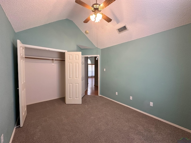 unfurnished bedroom with dark colored carpet, vaulted ceiling, a textured ceiling, a closet, and ceiling fan