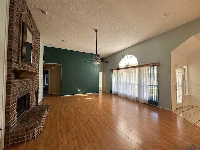 unfurnished living room with ceiling fan, hardwood / wood-style floors, a brick fireplace, and a textured ceiling