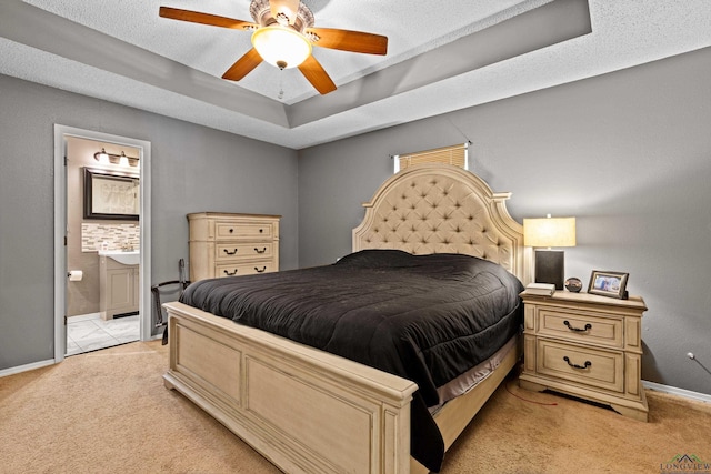 bedroom with baseboards, a raised ceiling, connected bathroom, and light carpet