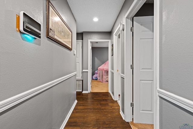 hall featuring baseboards, a textured wall, recessed lighting, and wood finished floors