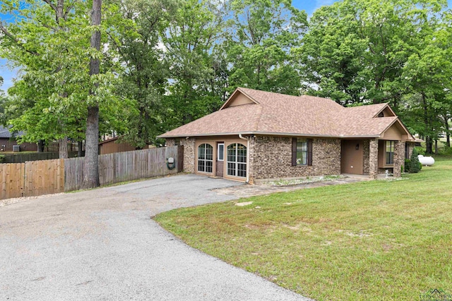 view of front of home featuring driveway, brick siding, fence, a front lawn, and a shingled roof