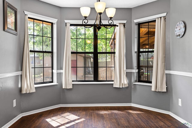 unfurnished dining area featuring baseboards, dark wood finished floors, and a chandelier