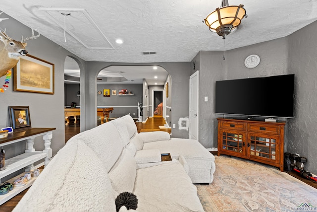 living area featuring arched walkways, a textured wall, recessed lighting, and visible vents