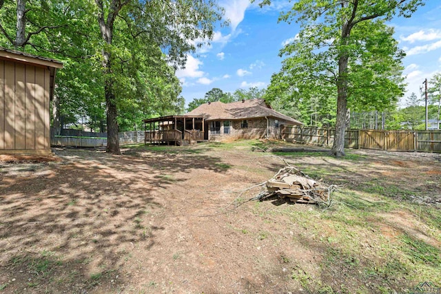 view of yard with a wooden deck, a fenced backyard, and a sunroom