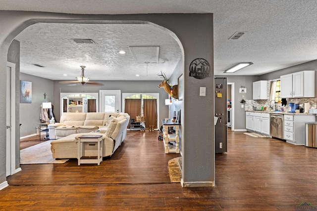 living area with arched walkways, a ceiling fan, dark wood finished floors, and visible vents