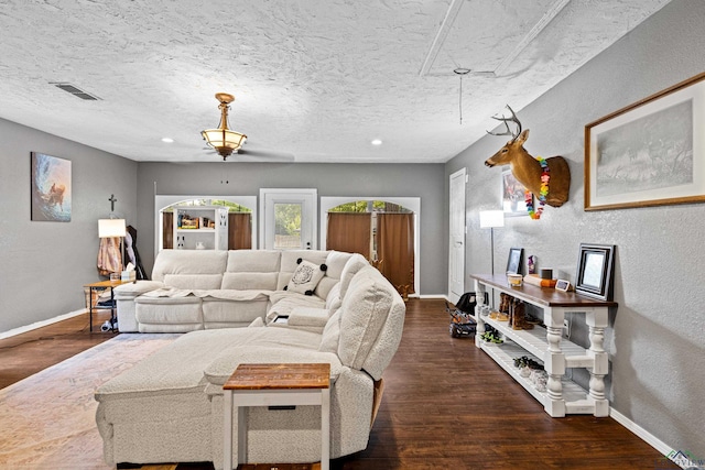 living room with a textured wall, attic access, baseboards, wood finished floors, and visible vents