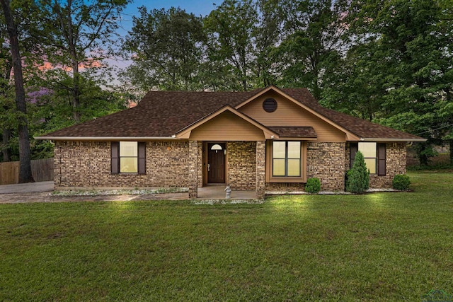 ranch-style home with a yard, brick siding, fence, and a shingled roof
