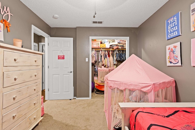carpeted bedroom featuring a textured ceiling, visible vents, a walk in closet, and a closet