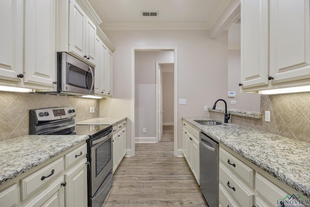 kitchen with white cabinetry, stainless steel appliances, light stone countertops, crown molding, and sink