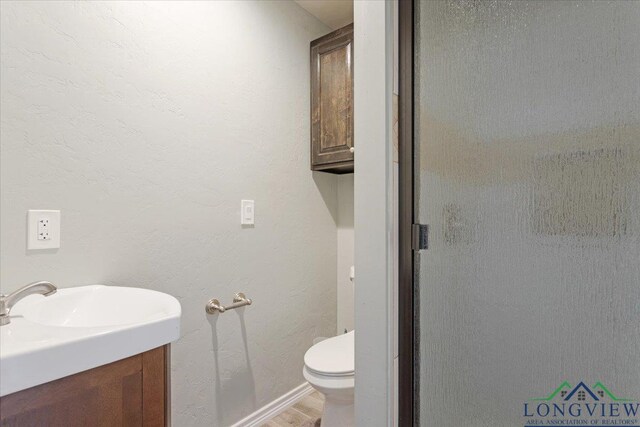 5796 Hwy 271 S, Pittsburg, TX 75686 - bathroom featuring toilet, wood finished floors, vanity, a shower with shower door, and baseboards