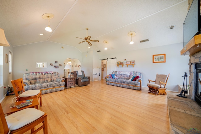 living room with hardwood / wood-style floors, lofted ceiling, a stone fireplace, ceiling fan, and a barn door