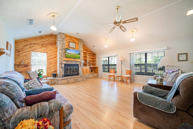 living room featuring ceiling fan, a stone fireplace, a textured ceiling, wooden walls, and hardwood / wood-style flooring