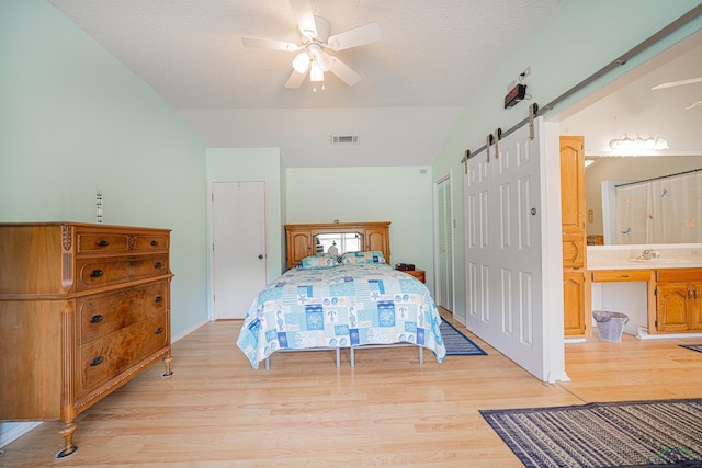 bedroom with ceiling fan, a barn door, ensuite bathroom, light hardwood / wood-style floors, and vaulted ceiling