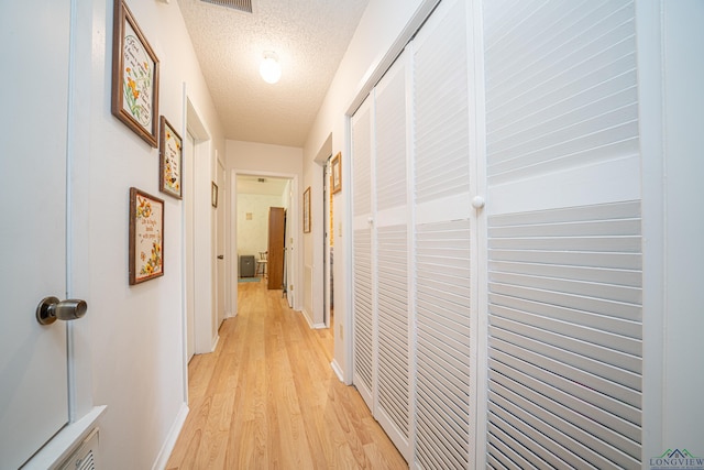 hall with a textured ceiling and light hardwood / wood-style floors